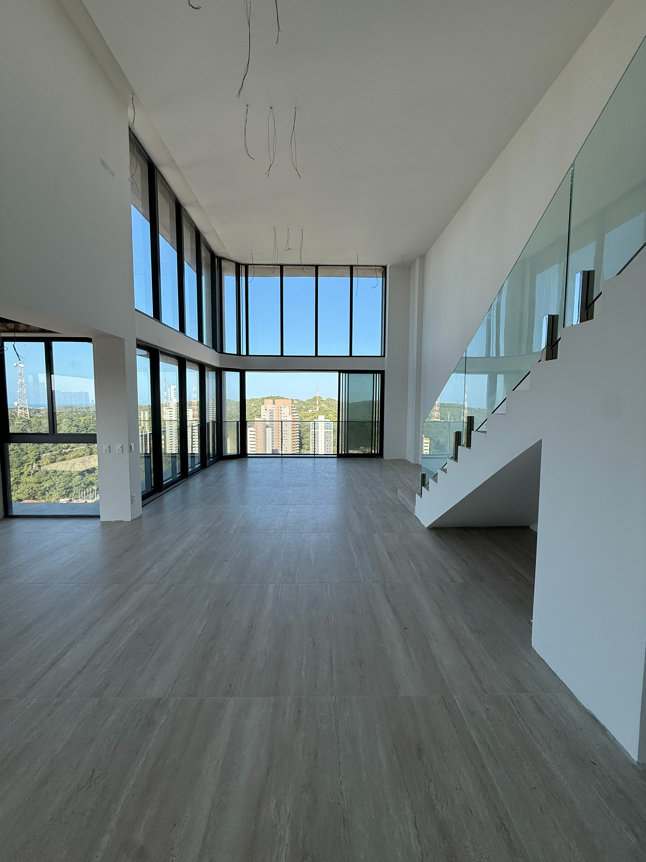 Sala de estar e jantar do imóvel em seu estado real, ainda inacabado, com piso assentado e esquadrias instaladas
