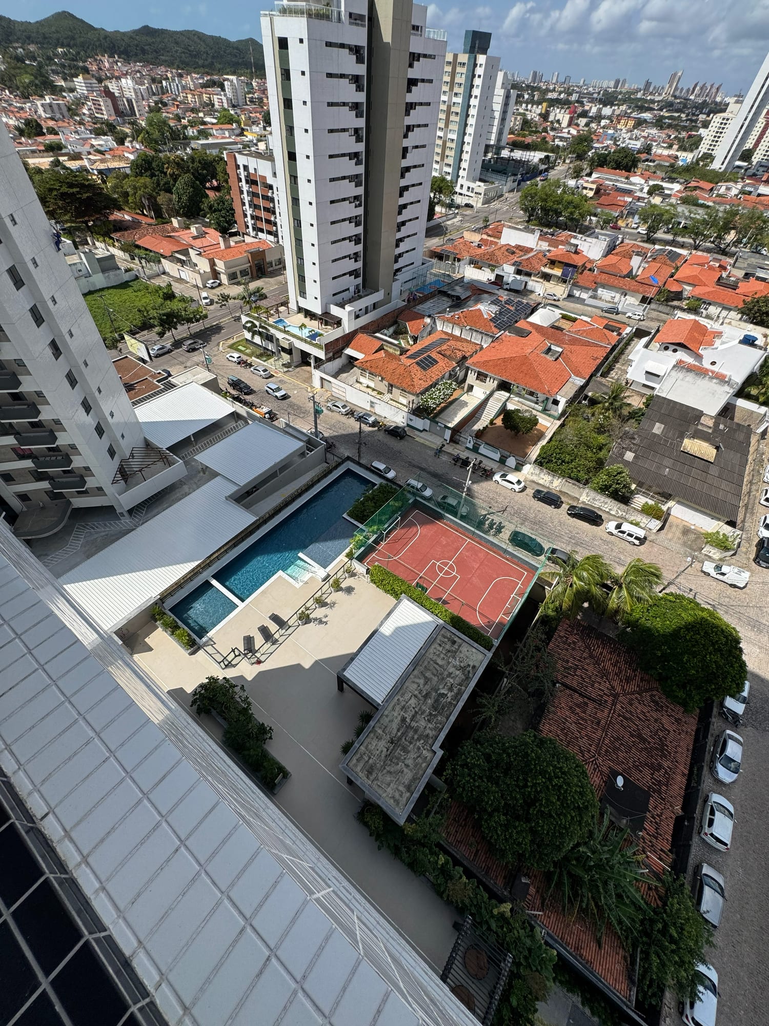 Piscina e quadra poliesportiva do Residencial Graciliano Ramos, vistas de cima, com a cidade de Natal ao fundo
